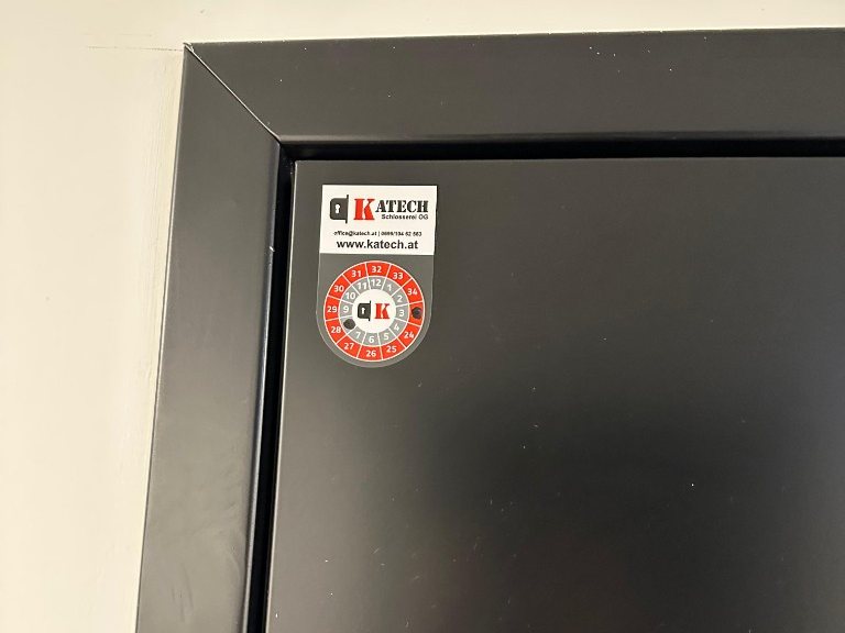 Prüfplakette von Katech an einer schwarzen Brandschutztür
