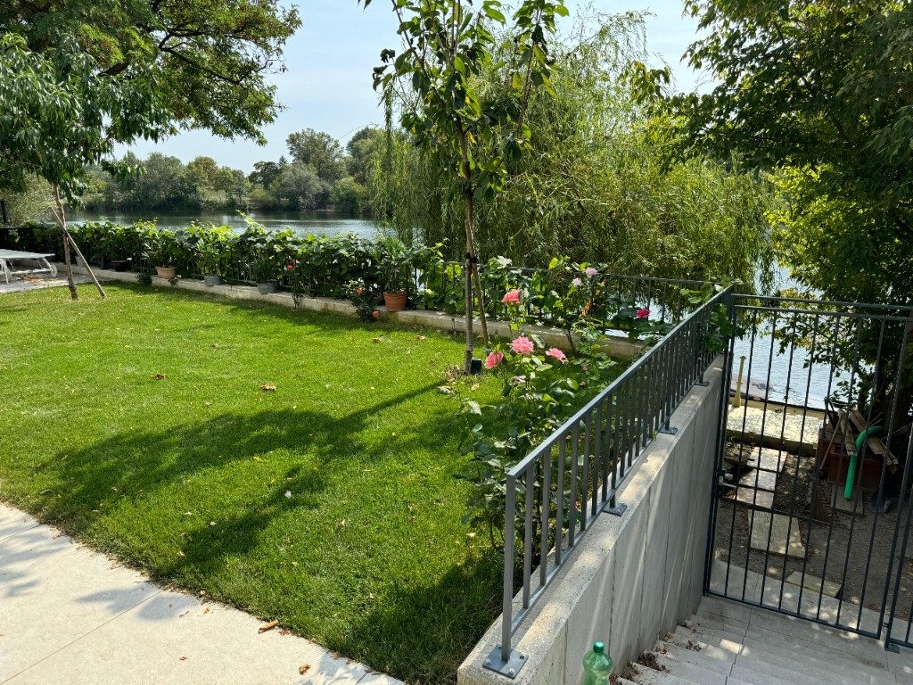 Dunkles Stabgeländer entlang einer Gartenmauer am Wasser