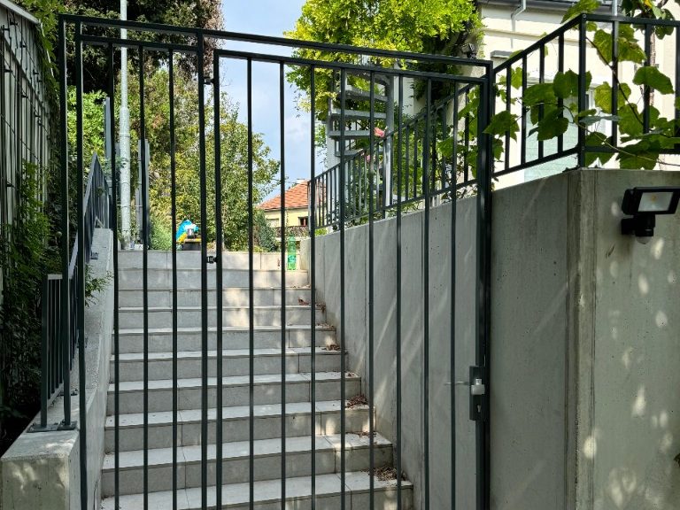 Anthrazitfarbenes Gittertor am oberen Ende einer Betontreppe